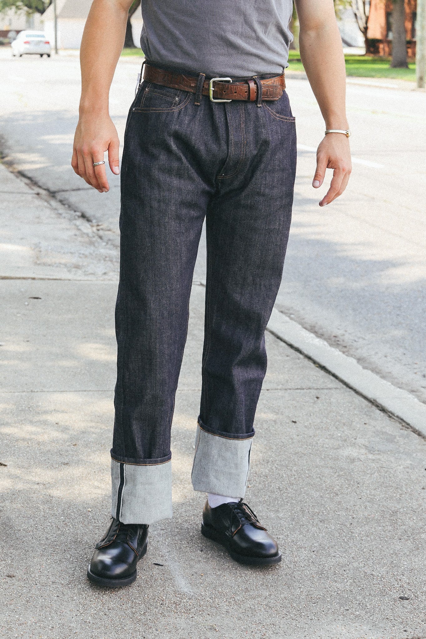 Man wearing dark selvedge denim jeans cuffed above black leather boots on a city sidewalk