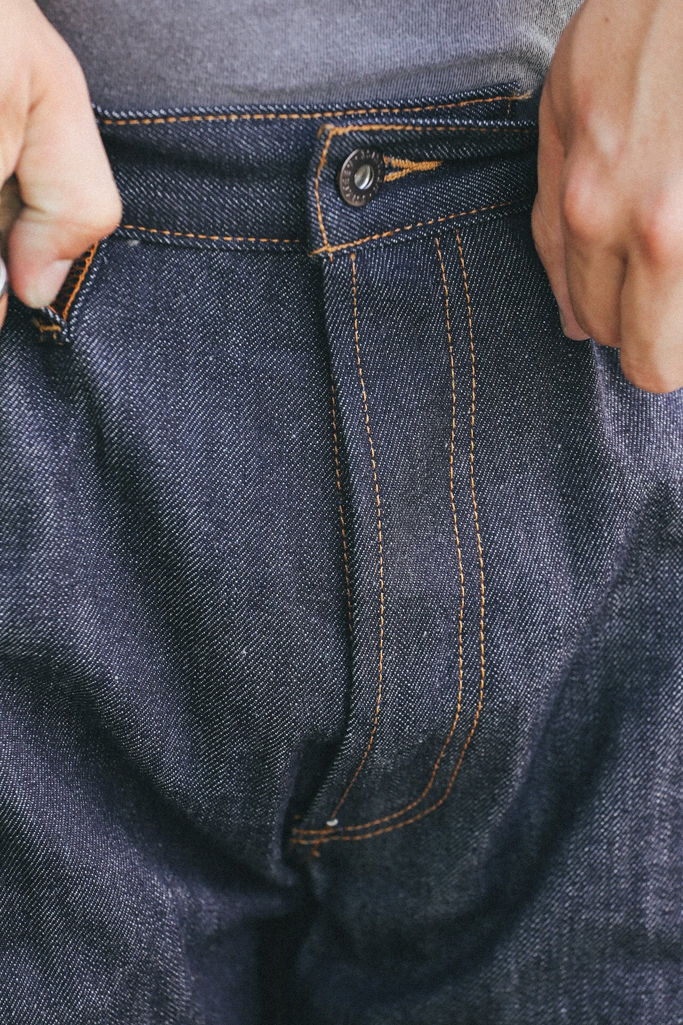Close-up of dark indigo raw denim jeans with contrast orange stitching and metal button fly closure