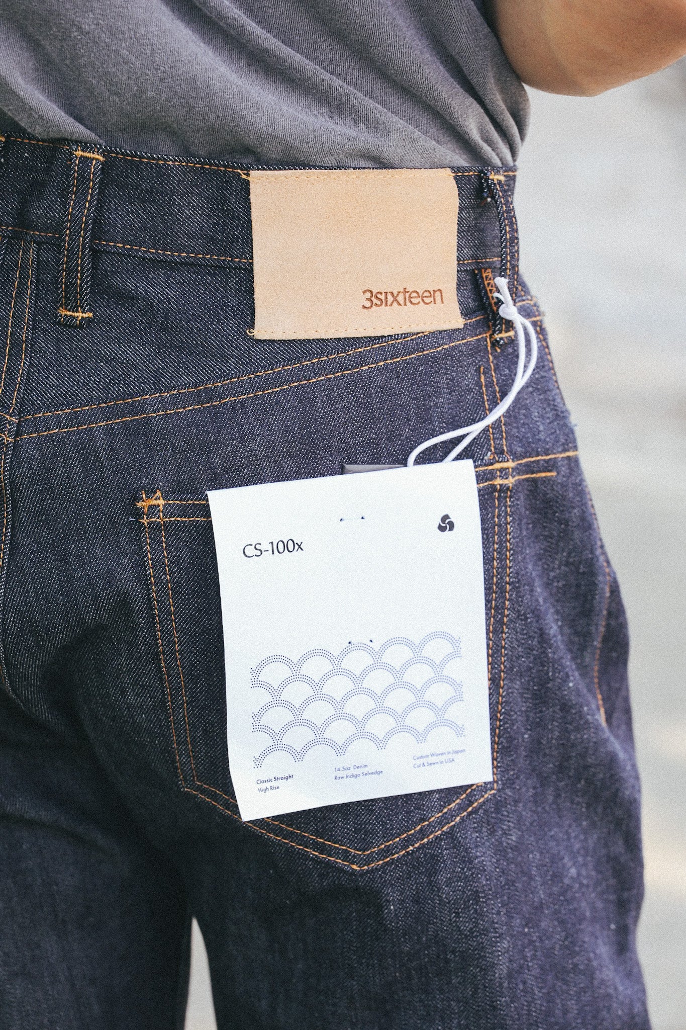 Close-up of dark indigo 3sixteen denim jeans with tan leather patch and white product tag on back pocket