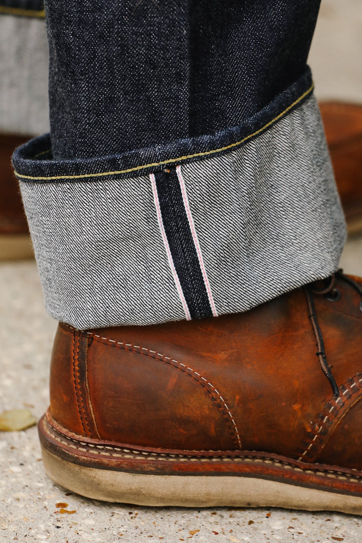 Close-up of a brown leather boot with rolled-up jeans showing a gray sock.
