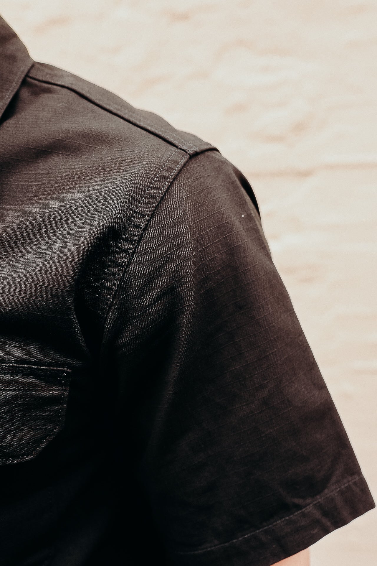 Close-up of a black work shirt sleeve with visible stitching detail against a light brick background
