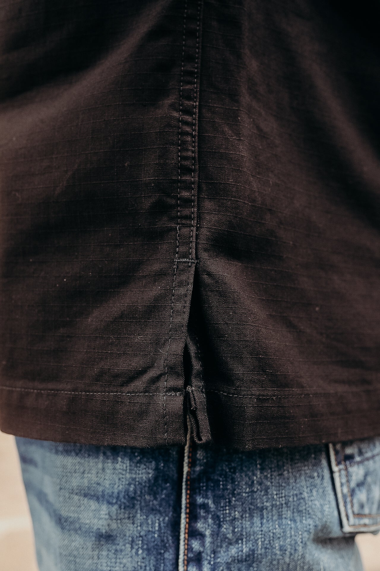 Close-up of a black cotton shirt hem with side slit over blue denim jeans, durable workwear detail