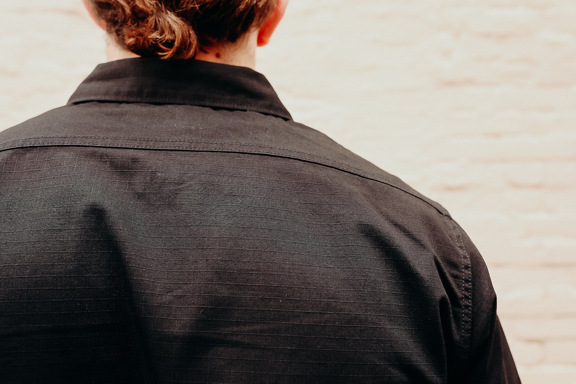 Back view of person wearing black textured work shirt against light brick wall