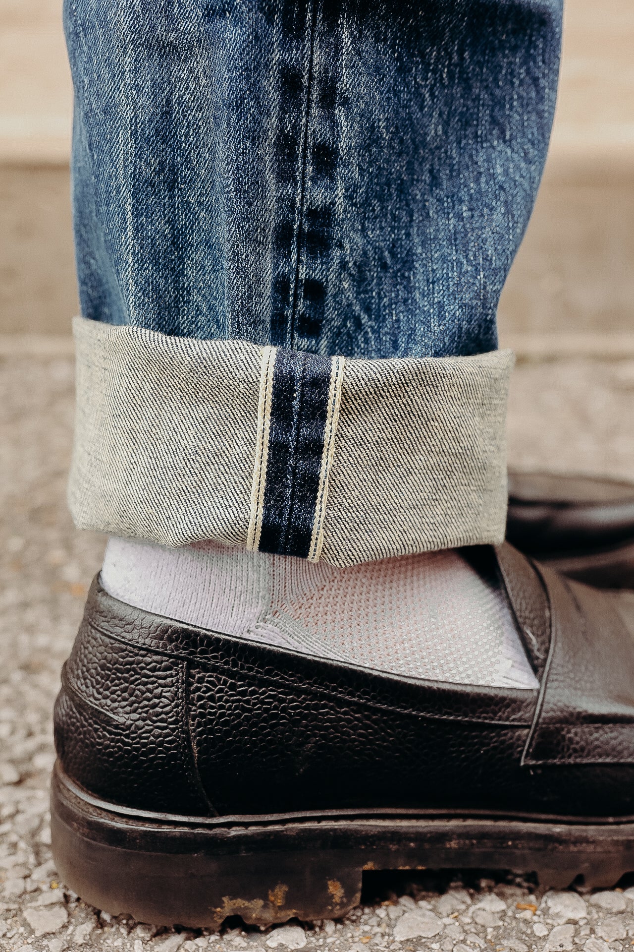 Close-up of rolled cuff blue denim jeans worn with white socks and black textured leather shoe
