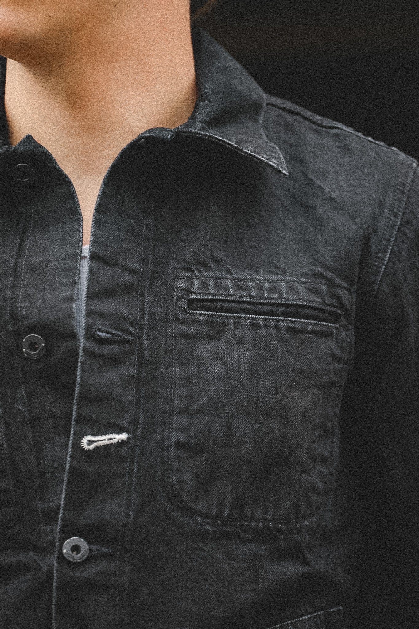 Close-up of a person wearing a dark denim jacket with a pocket on a black background