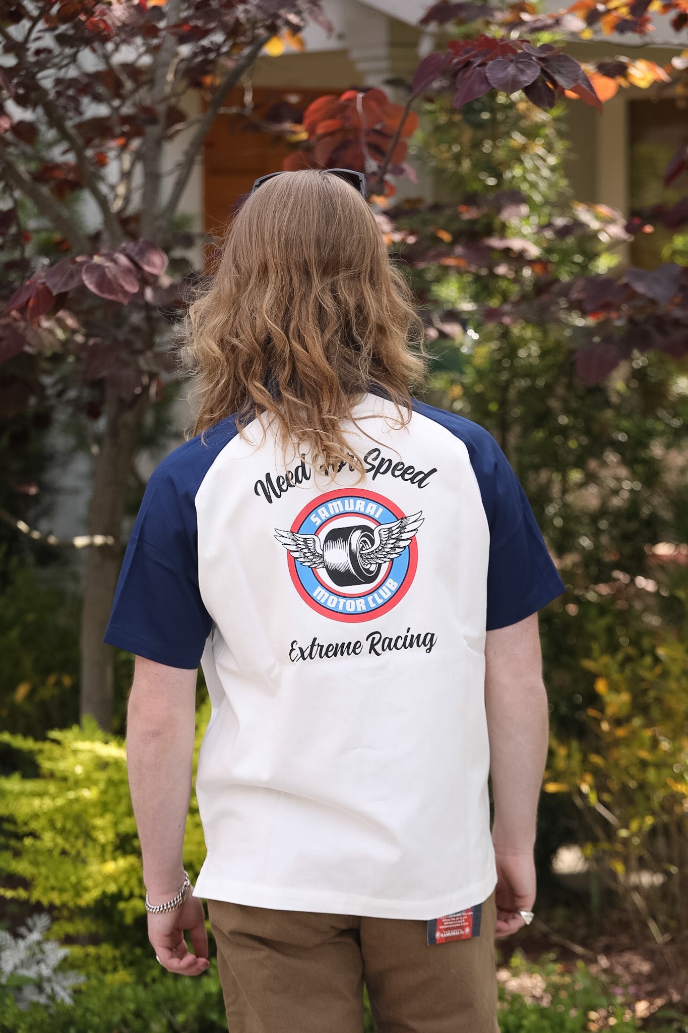 Person wearing a white and blue baseball shirt with a racing design outdoors.