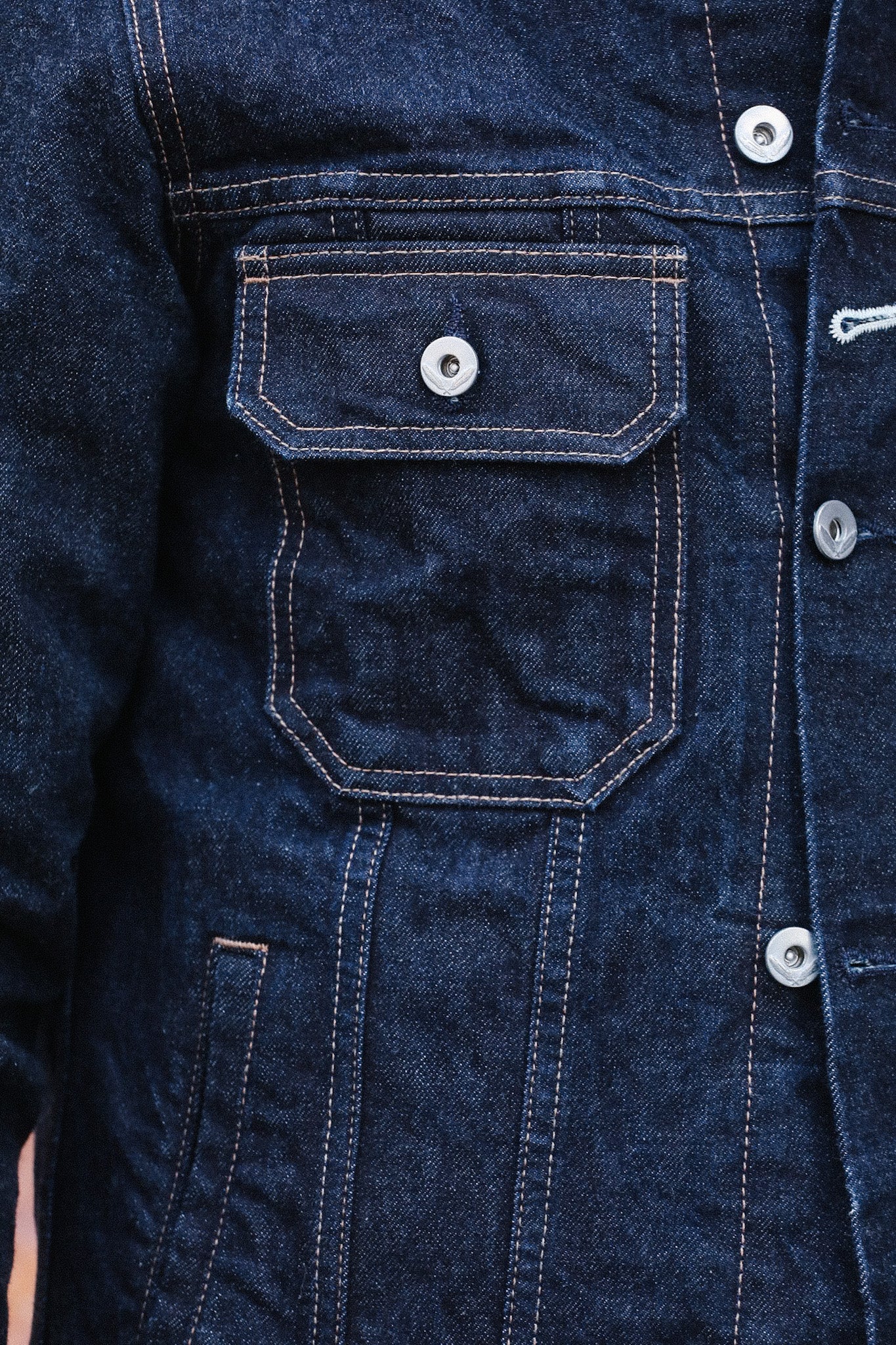 close-up of dark blue denim jacket pocket with silver buttons and contrast stitching