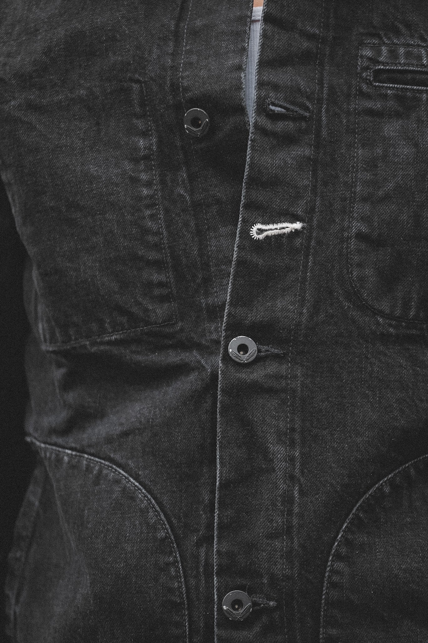 Close-up of a dark denim jacket with buttons and a zipper on a black background
