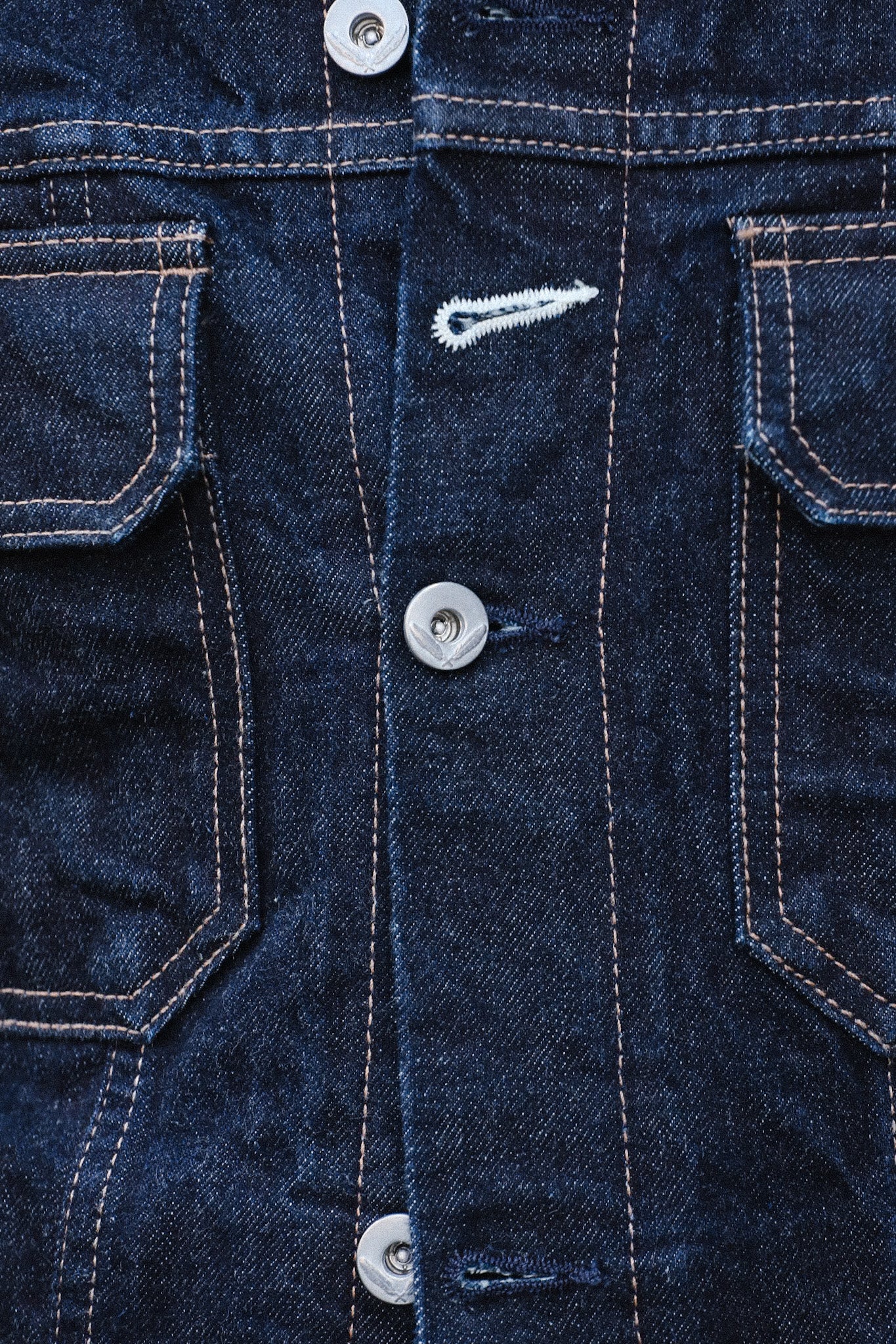 Close-up of dark blue denim jacket with metal buttons and contrasting orange stitching on pockets