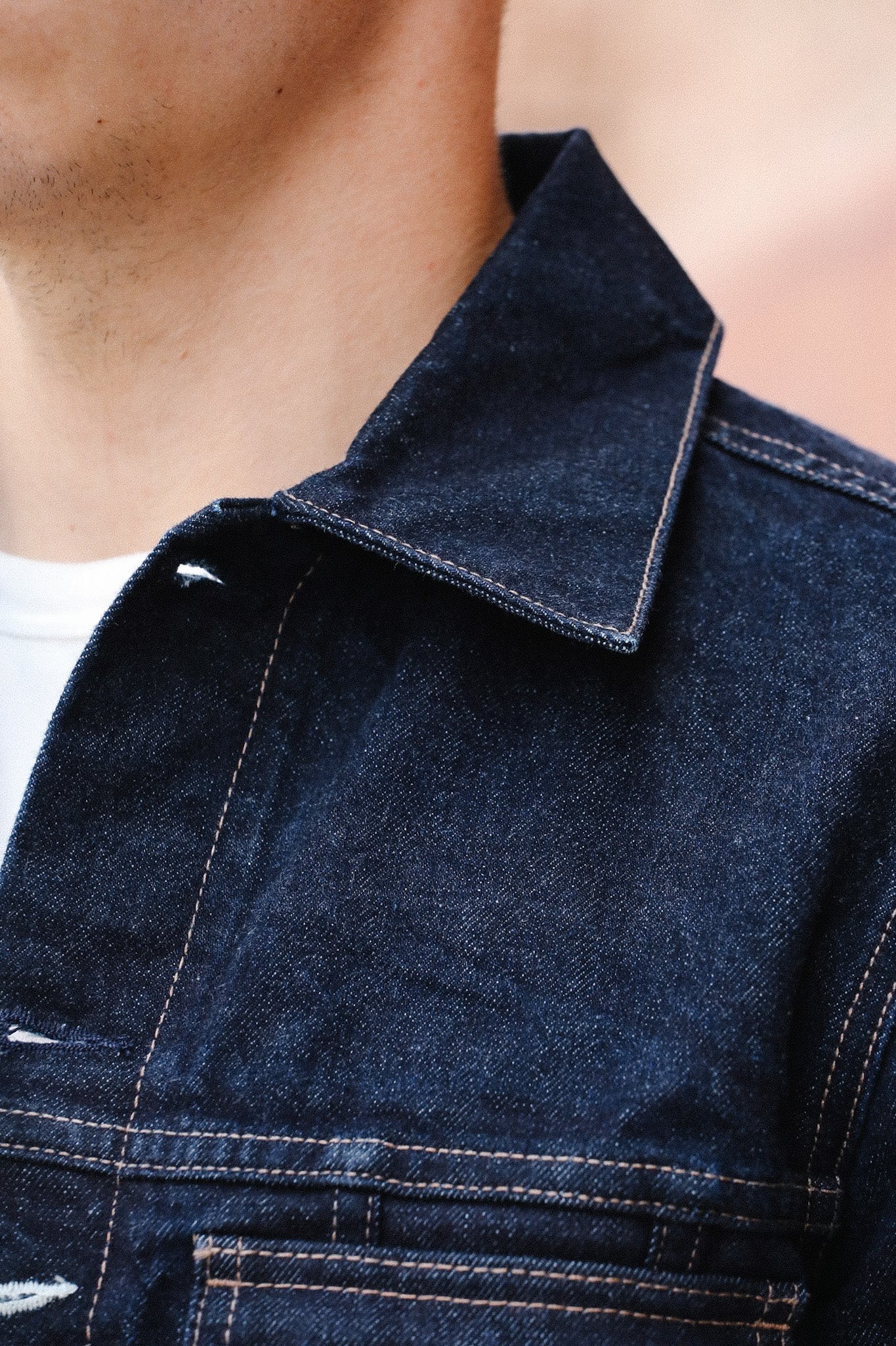 Close-up of a man wearing a dark blue denim jacket with tan stitching and a white shirt underneath