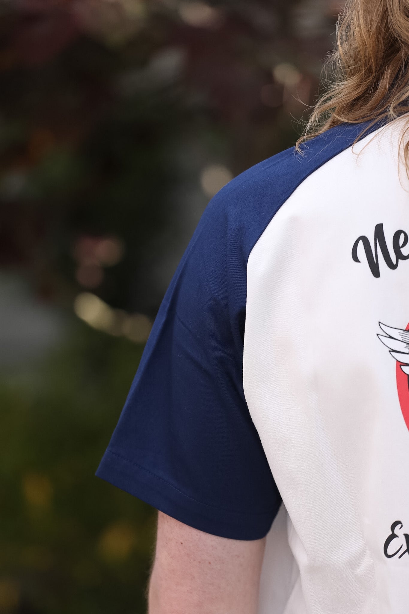 Person wearing a white and navy baseball shirt with text and graphics.