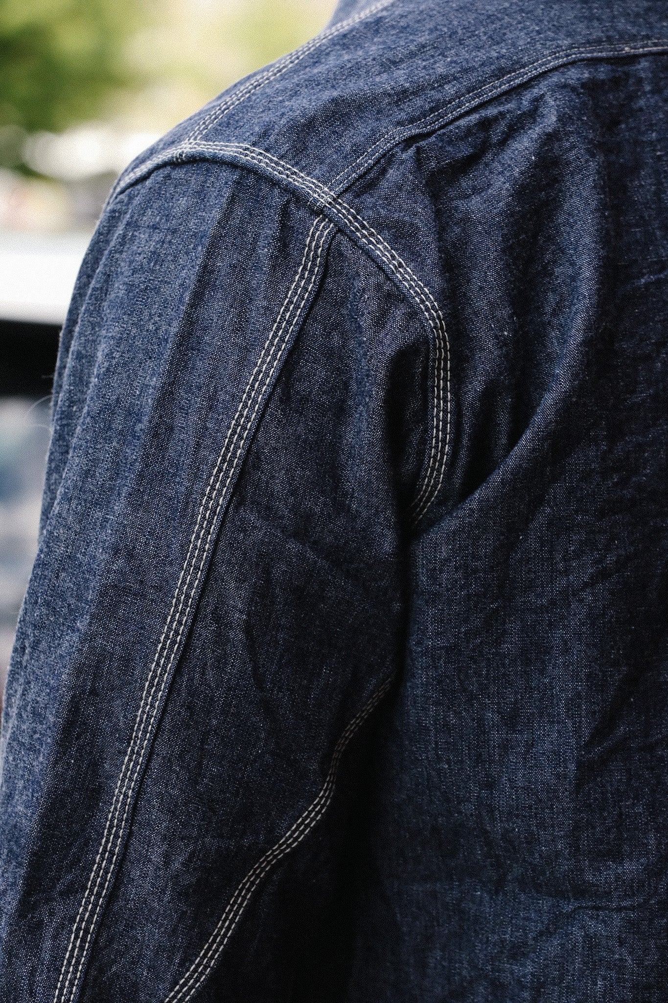 Close-up of dark blue denim jacket shoulder with contrasting white double stitching