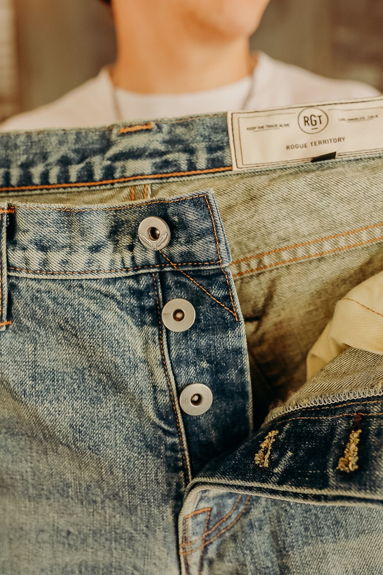 Close-up of hands holding Rogue Territory denim jeans with button fly and branded label