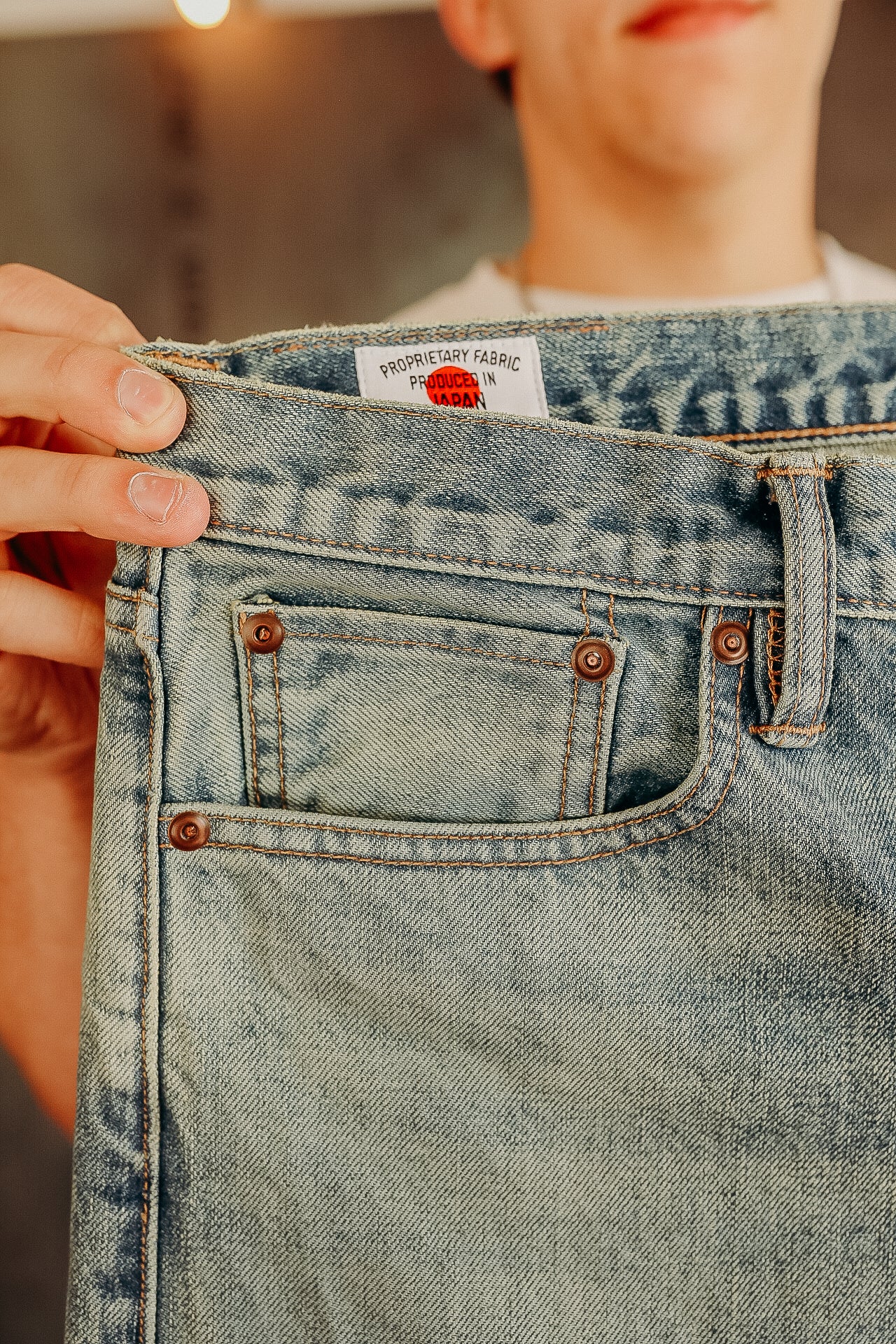 Close-up of light blue denim jeans pocket with copper rivets and label indicating fabric produced in Japan