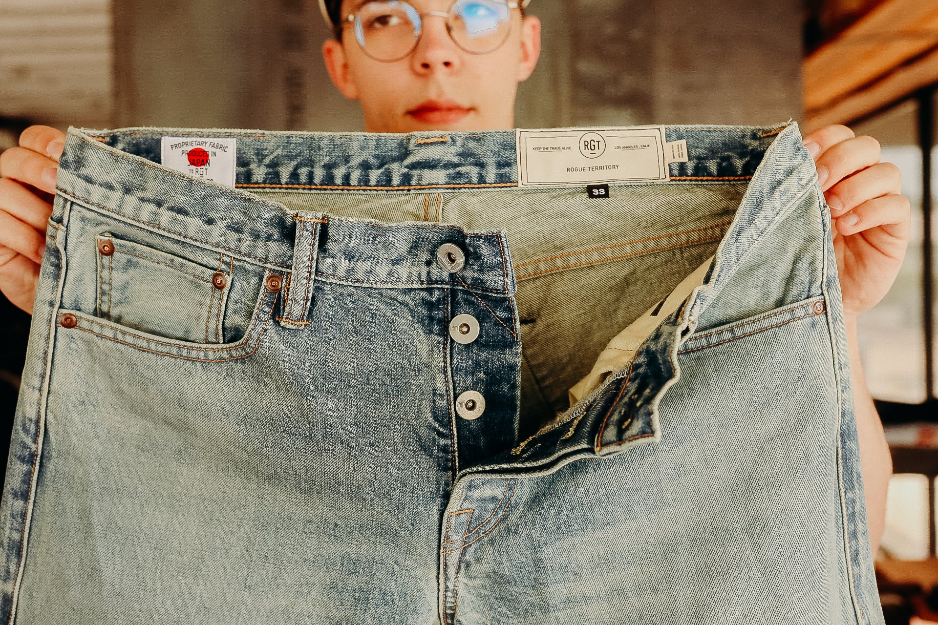 Person holding light blue Rogue Territory denim jeans with visible button fly and brand labels