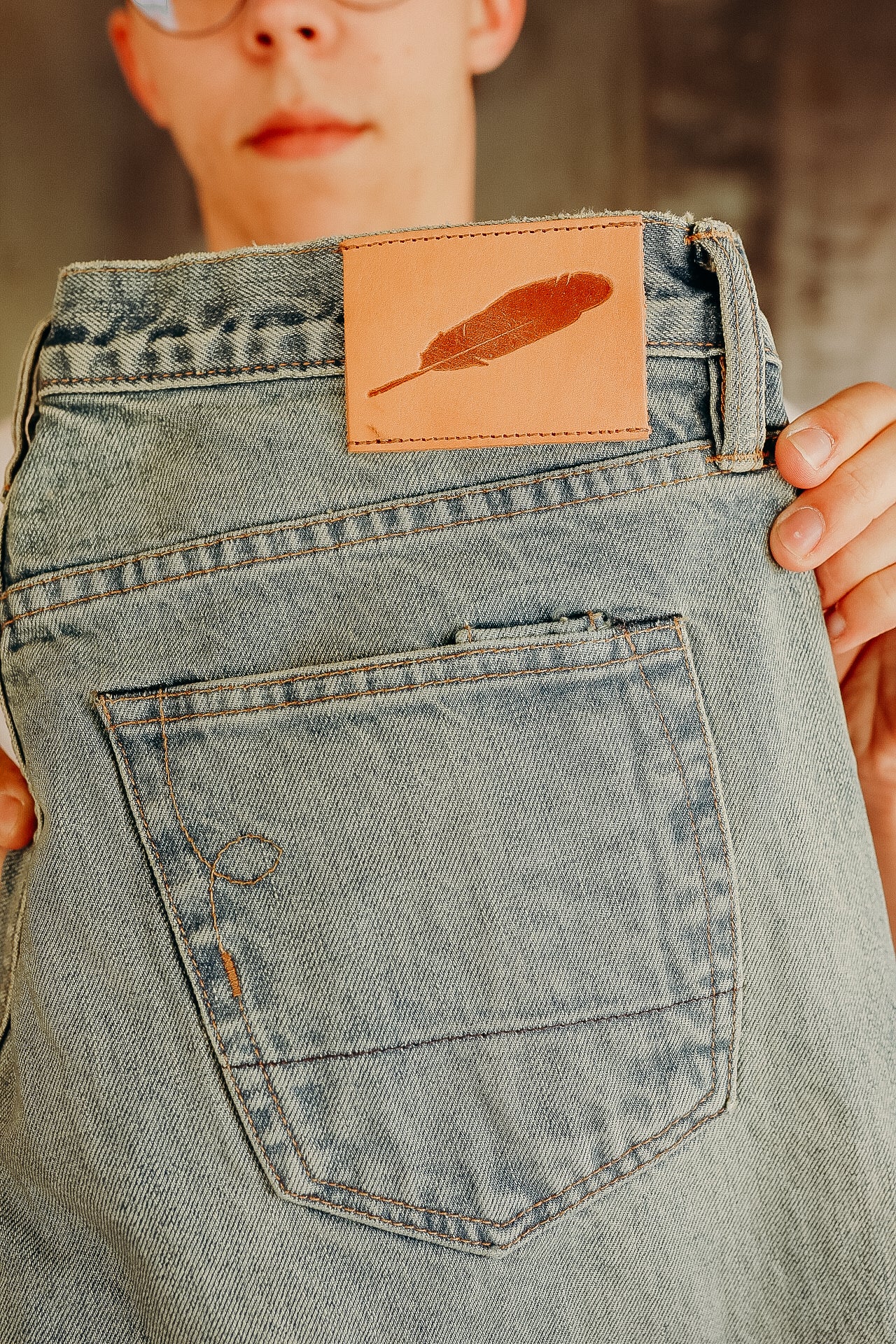 Close-up of light blue denim jeans back pocket and leather patch with feather logo held by a person