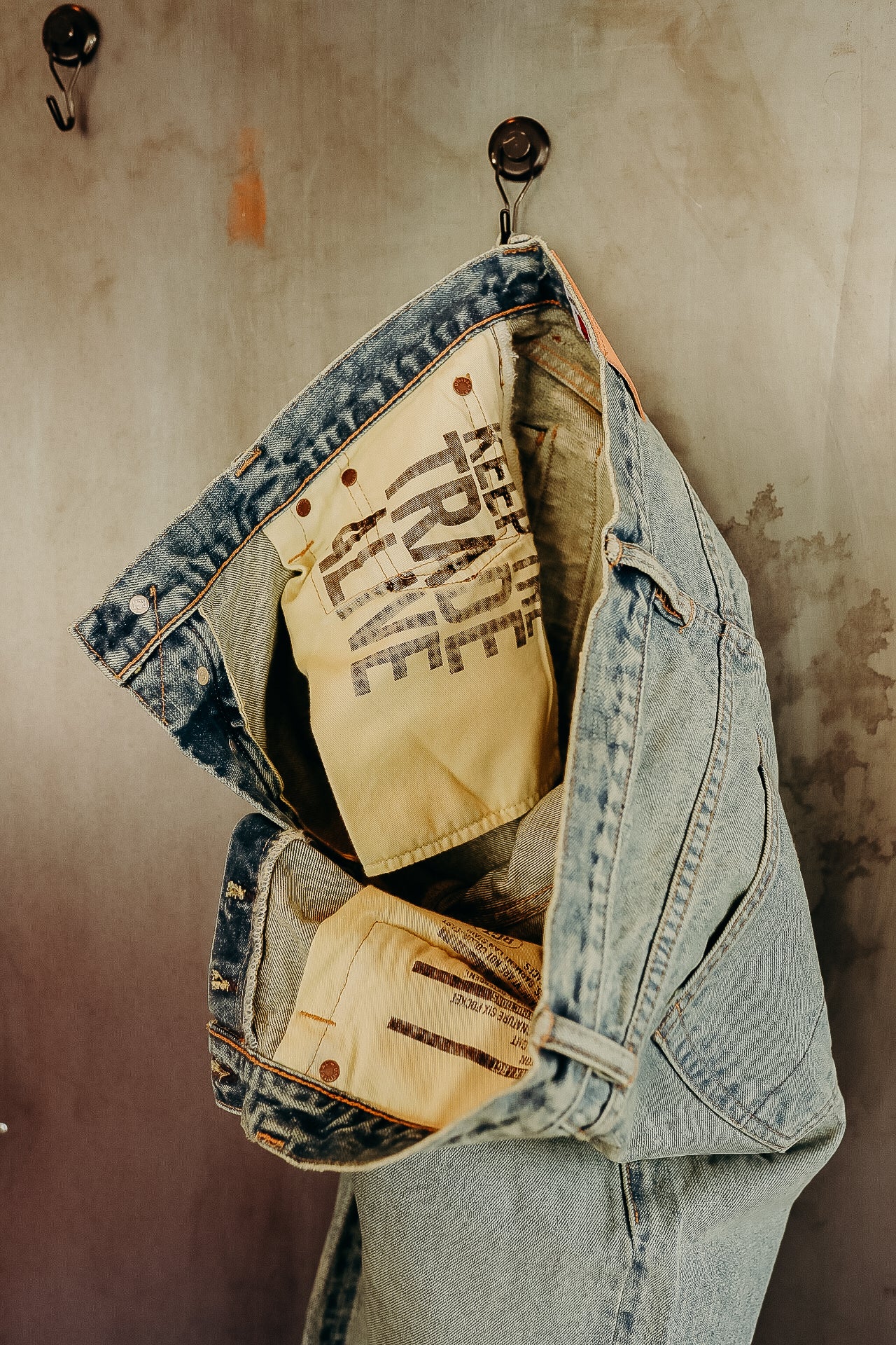 Light blue denim jeans hanging on metal hooks showing inside label with Keep Trade Alive text
