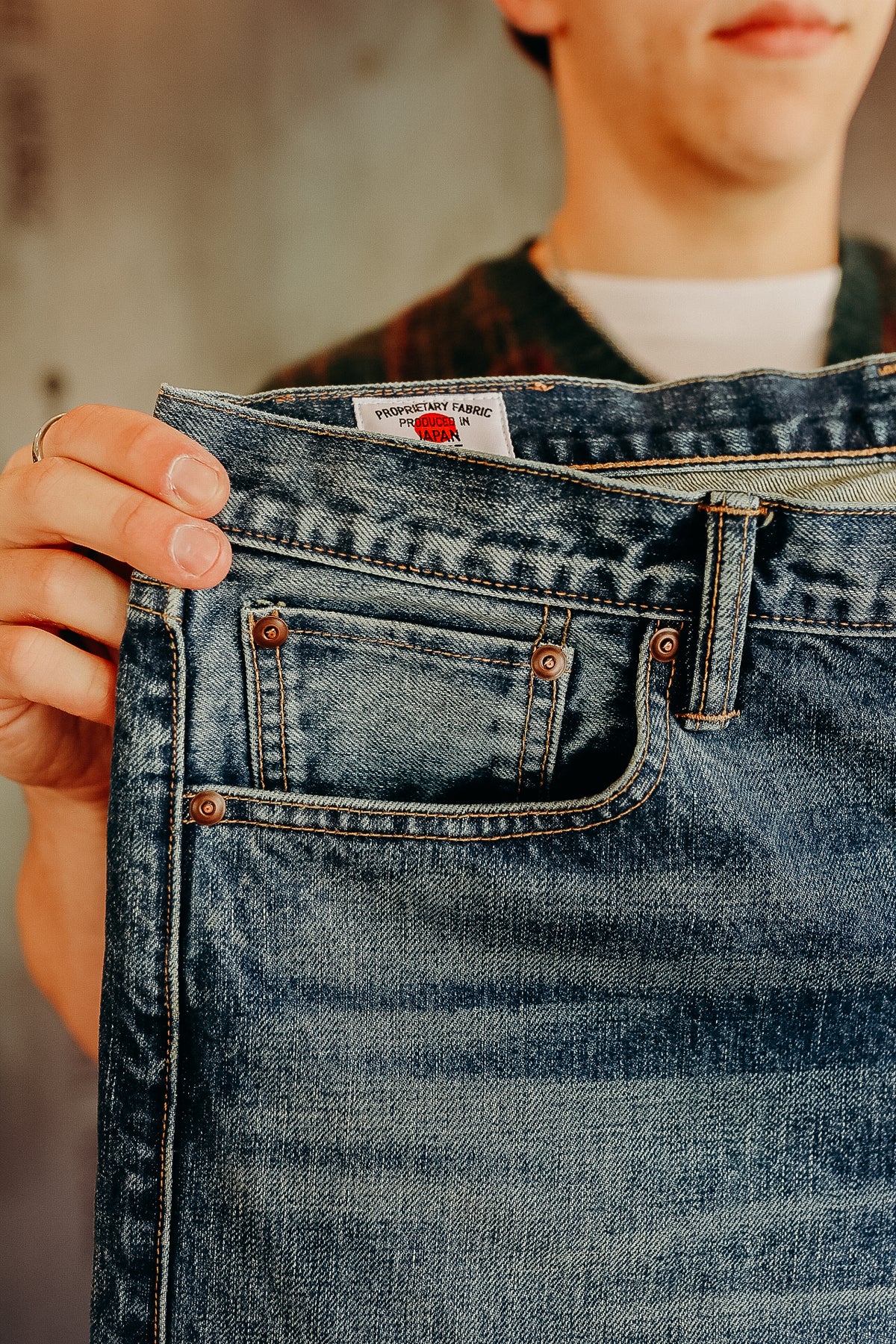 Close-up of hands holding blue denim jeans with visible Japan-made fabric label at Iron Shop Provisions