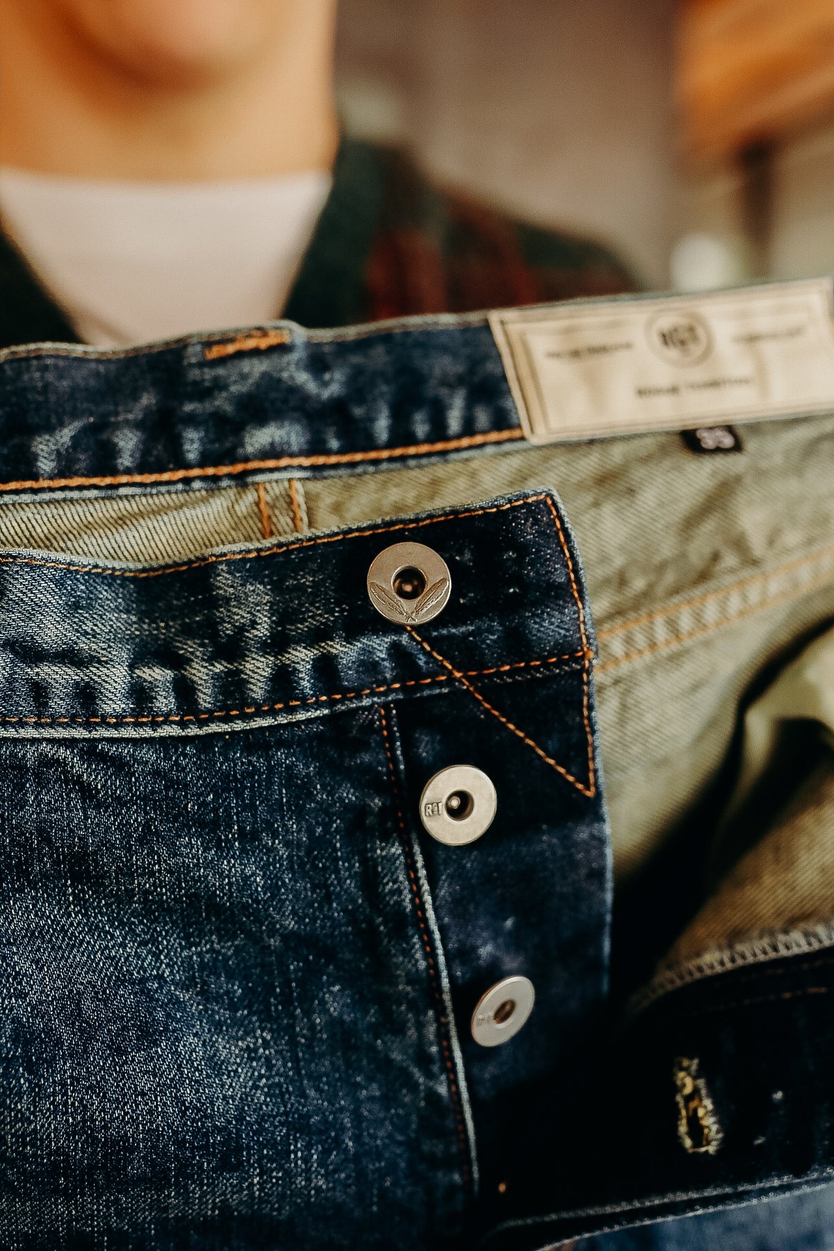 Close-up of dark blue denim jeans with metal buttons and orange stitching at Iron Shop Provisions