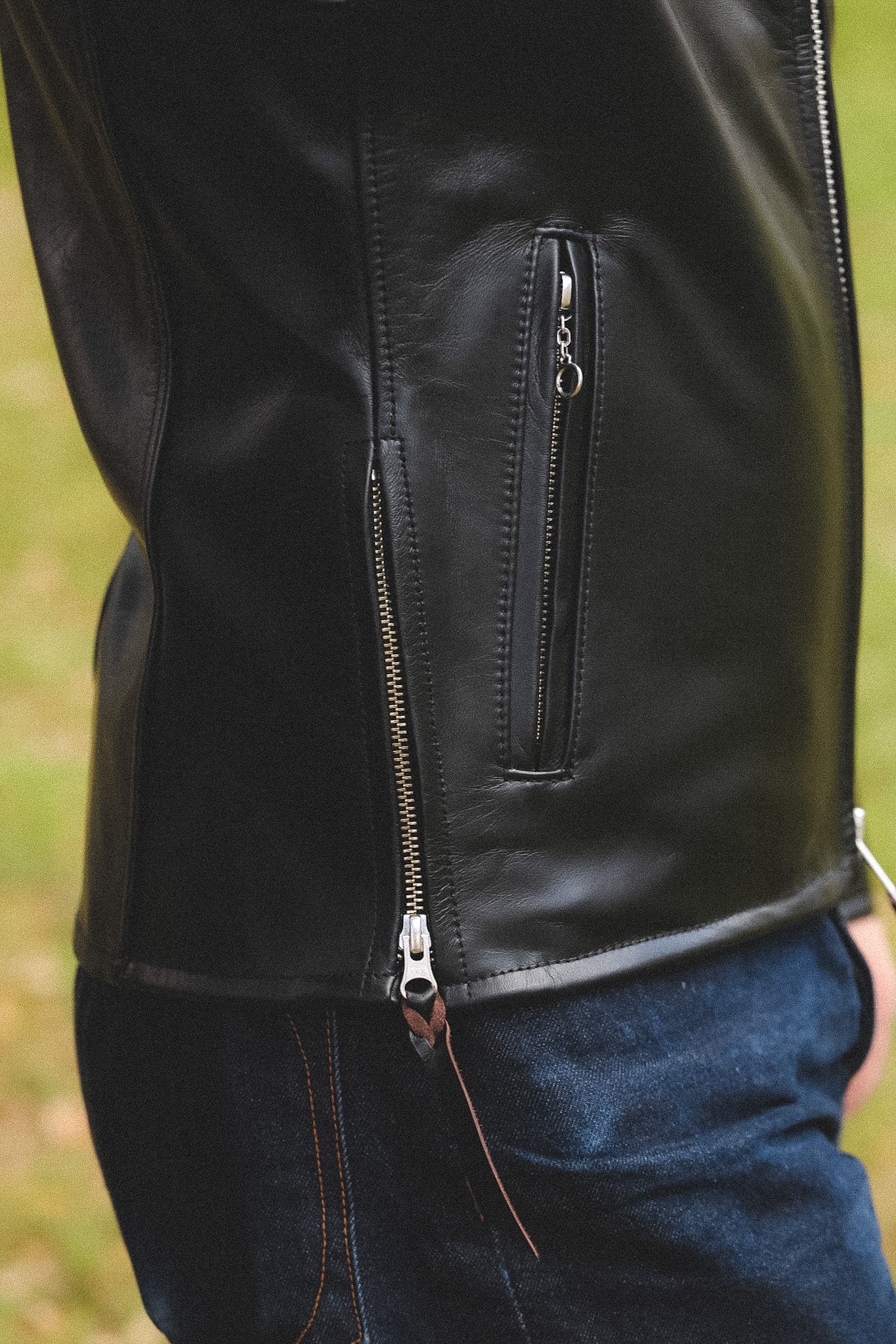 A person wearing a black horsehide rider's jacket with a collar, standing outdoors.