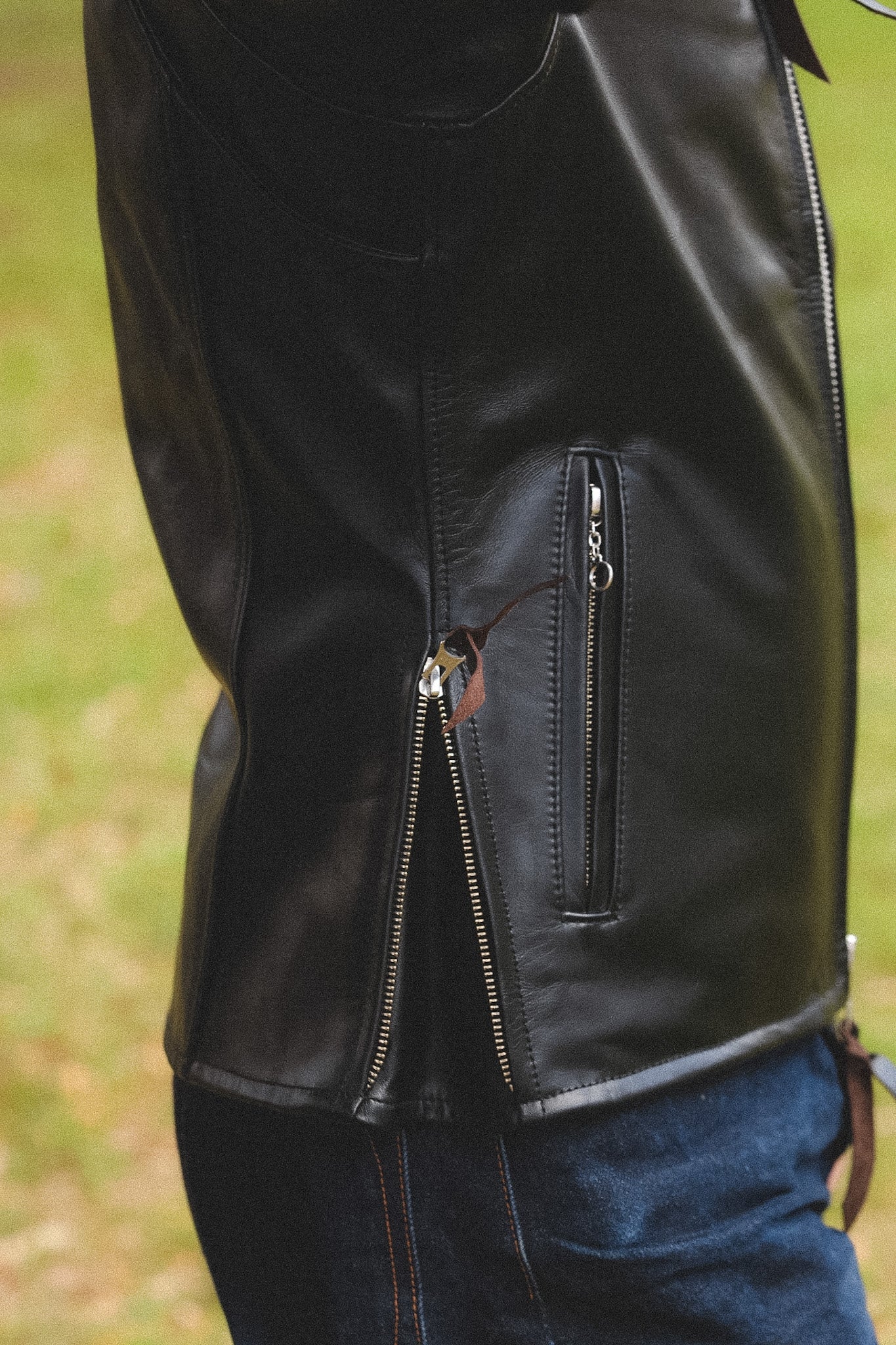 A person wearing a black horsehide rider's jacket with a collar, standing outdoors.