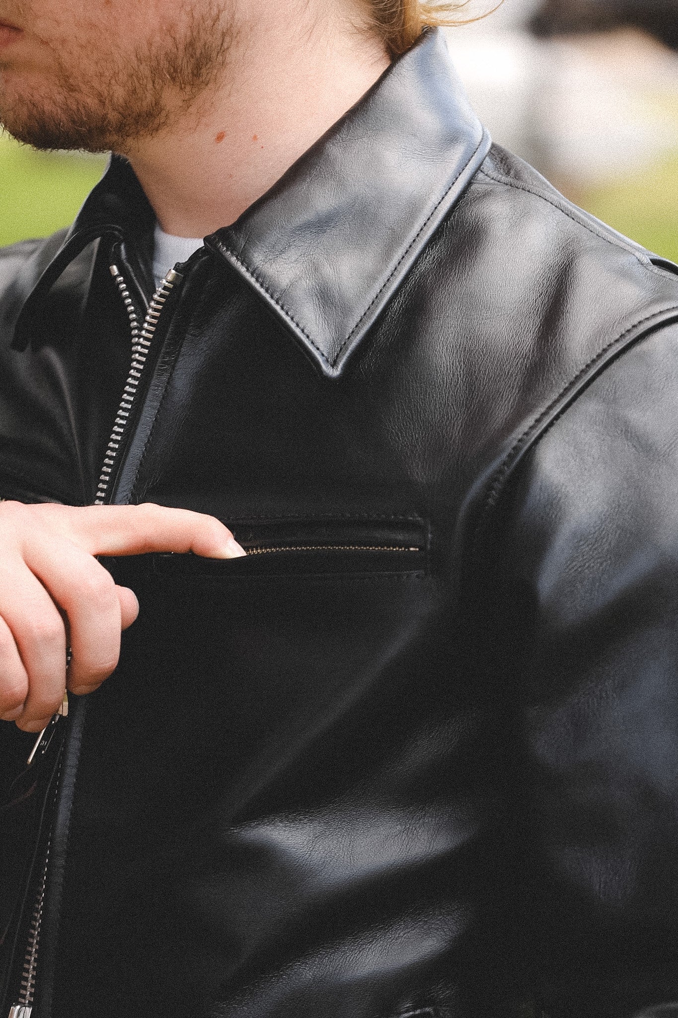 A person wearing a black horsehide rider's jacket with a collar, standing outdoors.