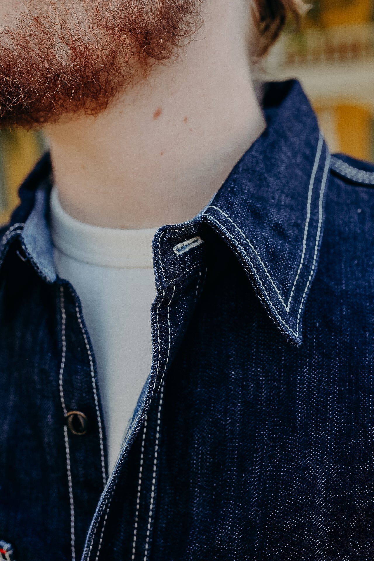 Close-up of a man wearing a dark blue denim jacket with white stitching over a white T-shirt