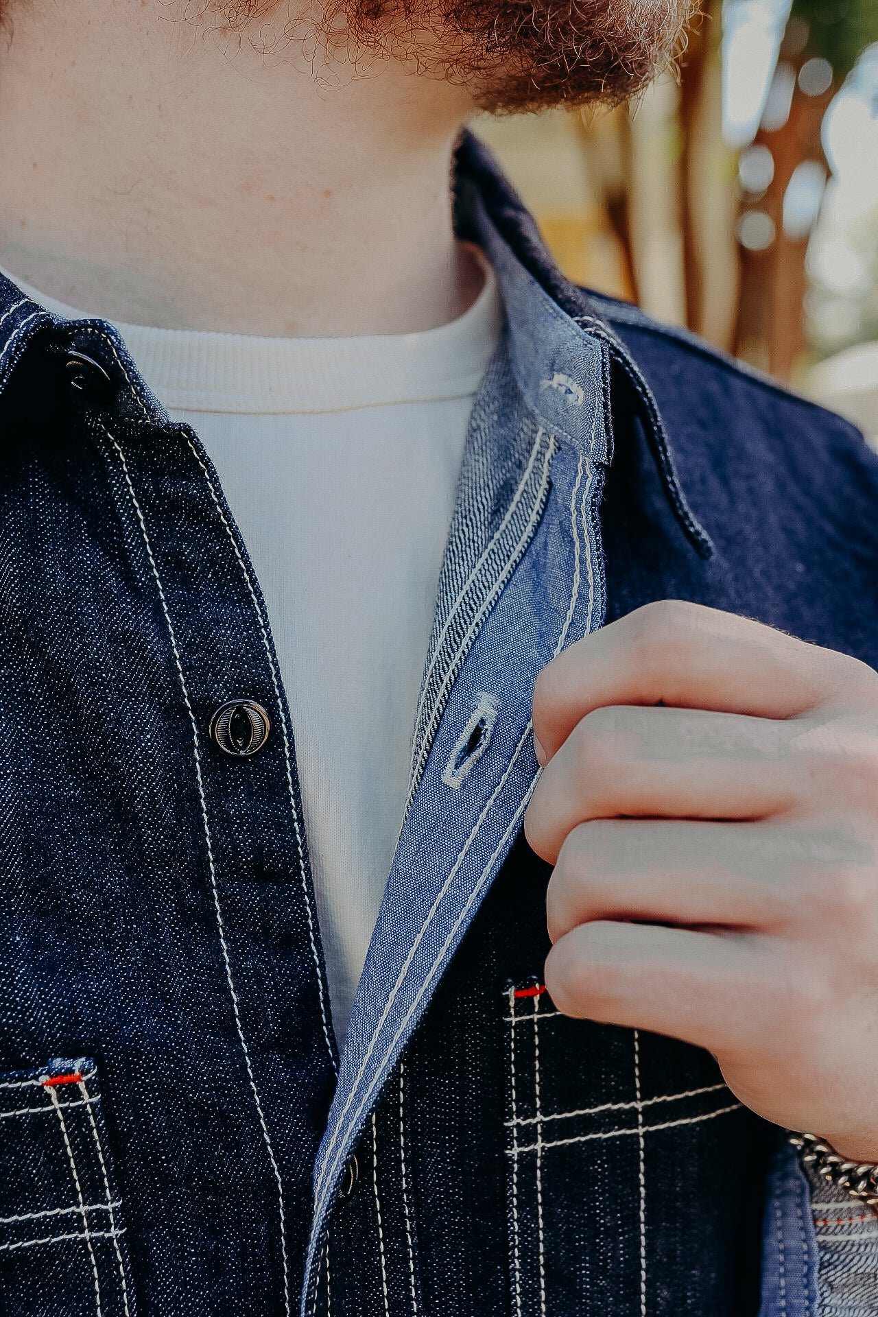 Close-up of a person with a beard wearing a dark denim jacket over a white shirt, unbuttoning the jacket