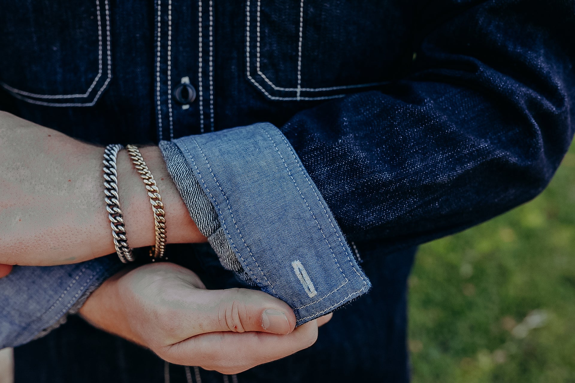 Person adjusting denim shirt cuff showing silver and gold chain bracelets