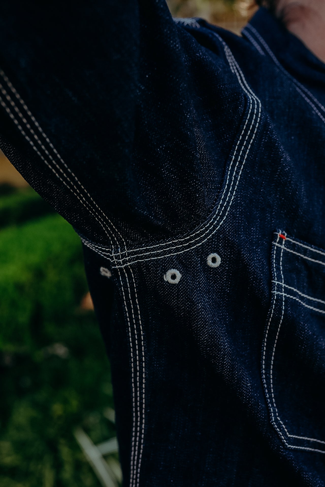 Close-up of durable dark blue denim fabric with white double stitching and metal eyelets, Iron Shop Provisions style