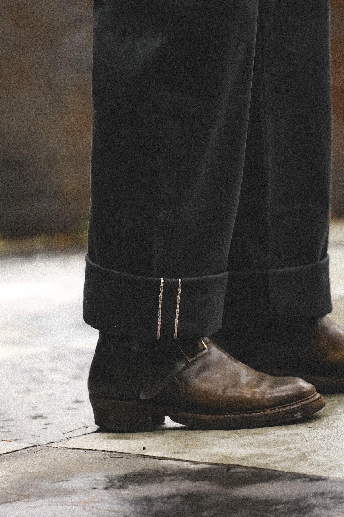 Close-up of brown leather shoes and black pants on a wooden floor.