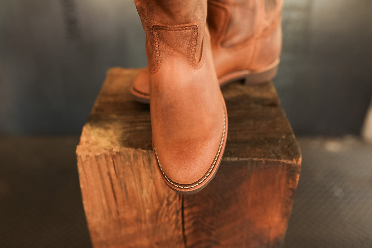 Brown leather boot on a wooden block with a blurred background