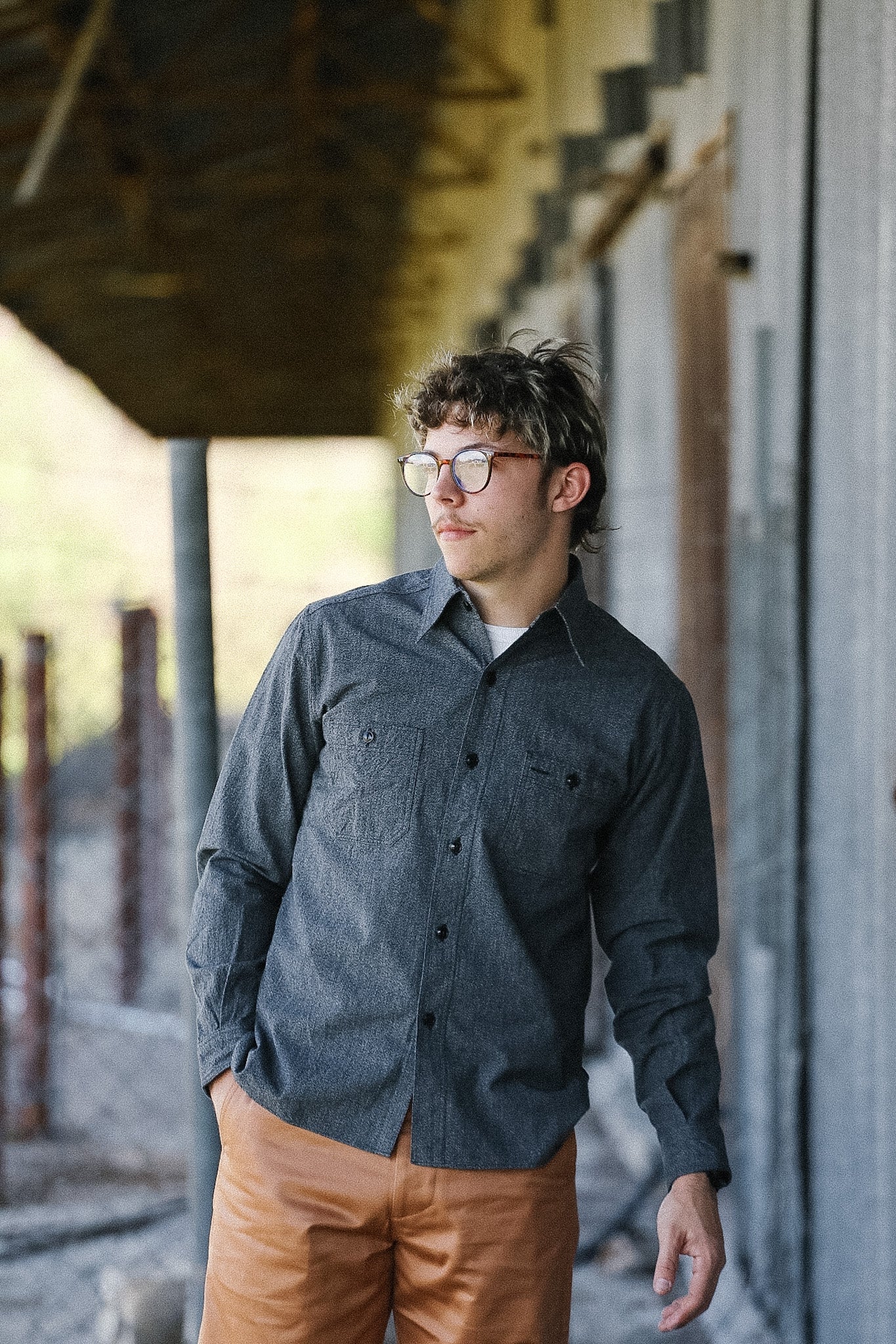 Man wearing a dark shirt and brown pants standing outdoors near a building.