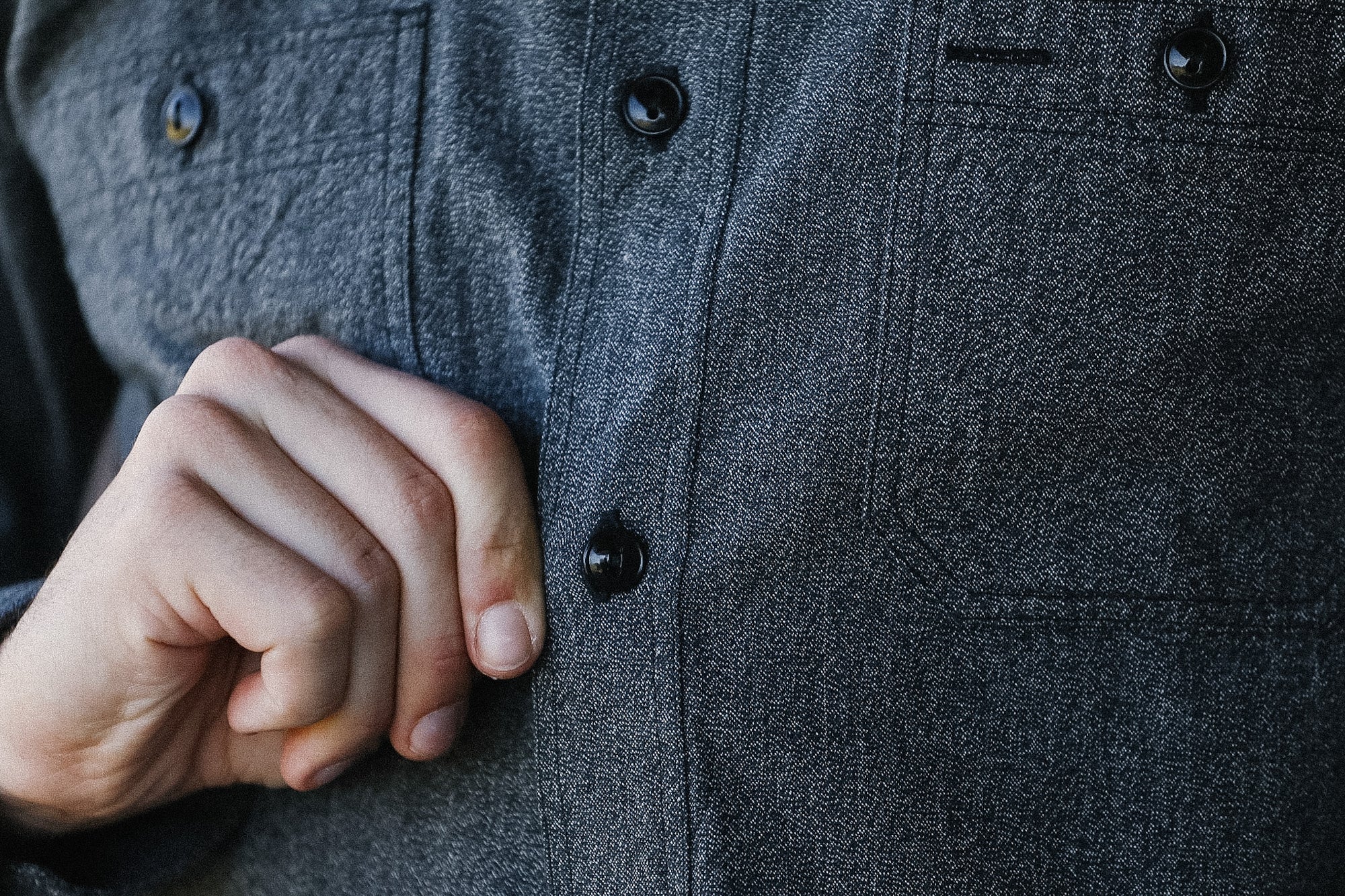 Close-up of a person wearing a dark gray button-up shirt with a hand adjusting a button.