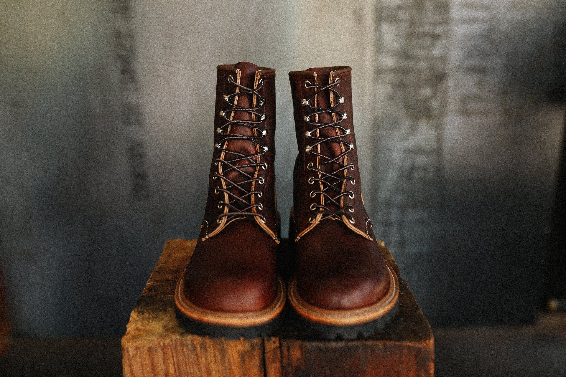 Pair of brown leather lace-up boots on wooden block in rustic setting, Iron Shop Provisions