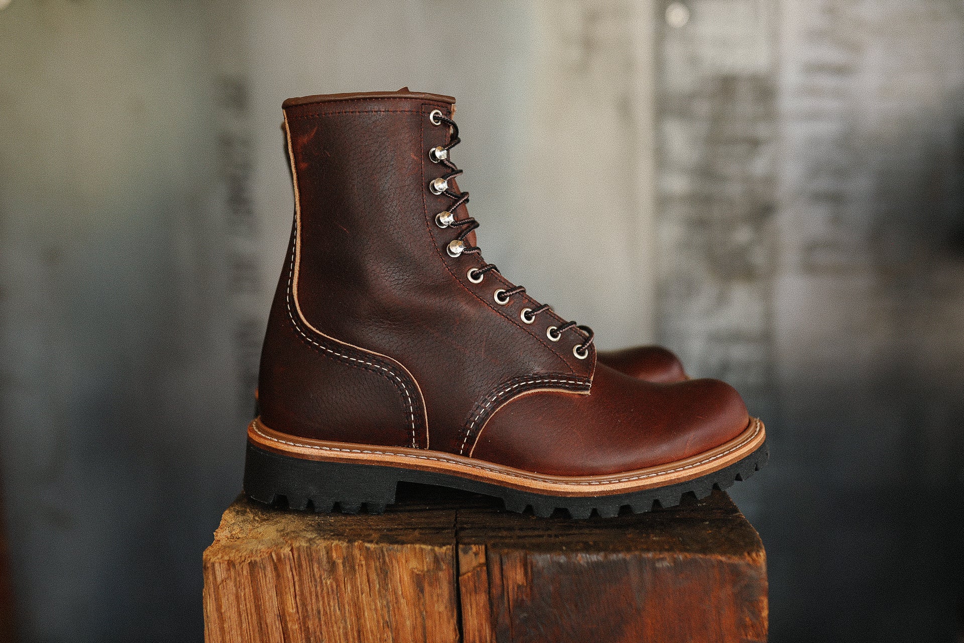 Brown leather lace-up work boot with rugged sole on wooden surface, industrial background