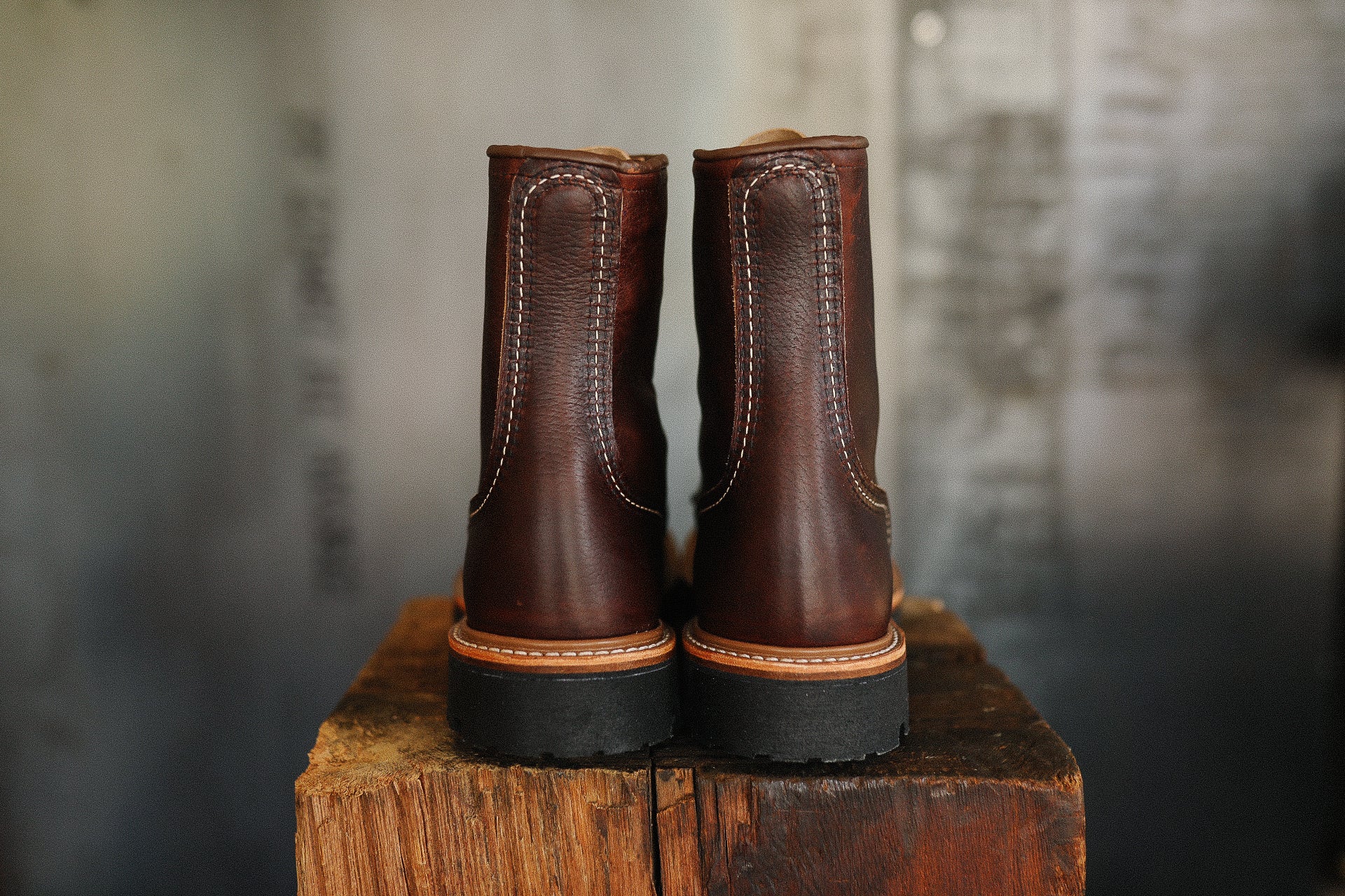 Back view of brown leather work boots with black soles on wooden surface