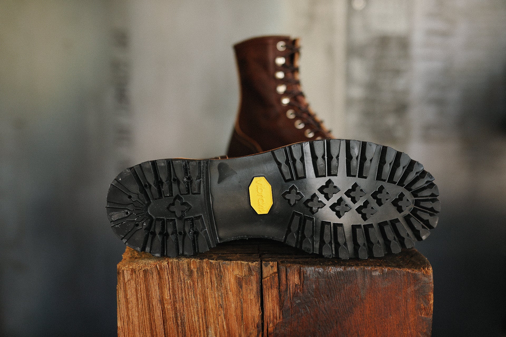 Close-up of black Vibram lug sole on brown leather boot resting on rustic wooden block