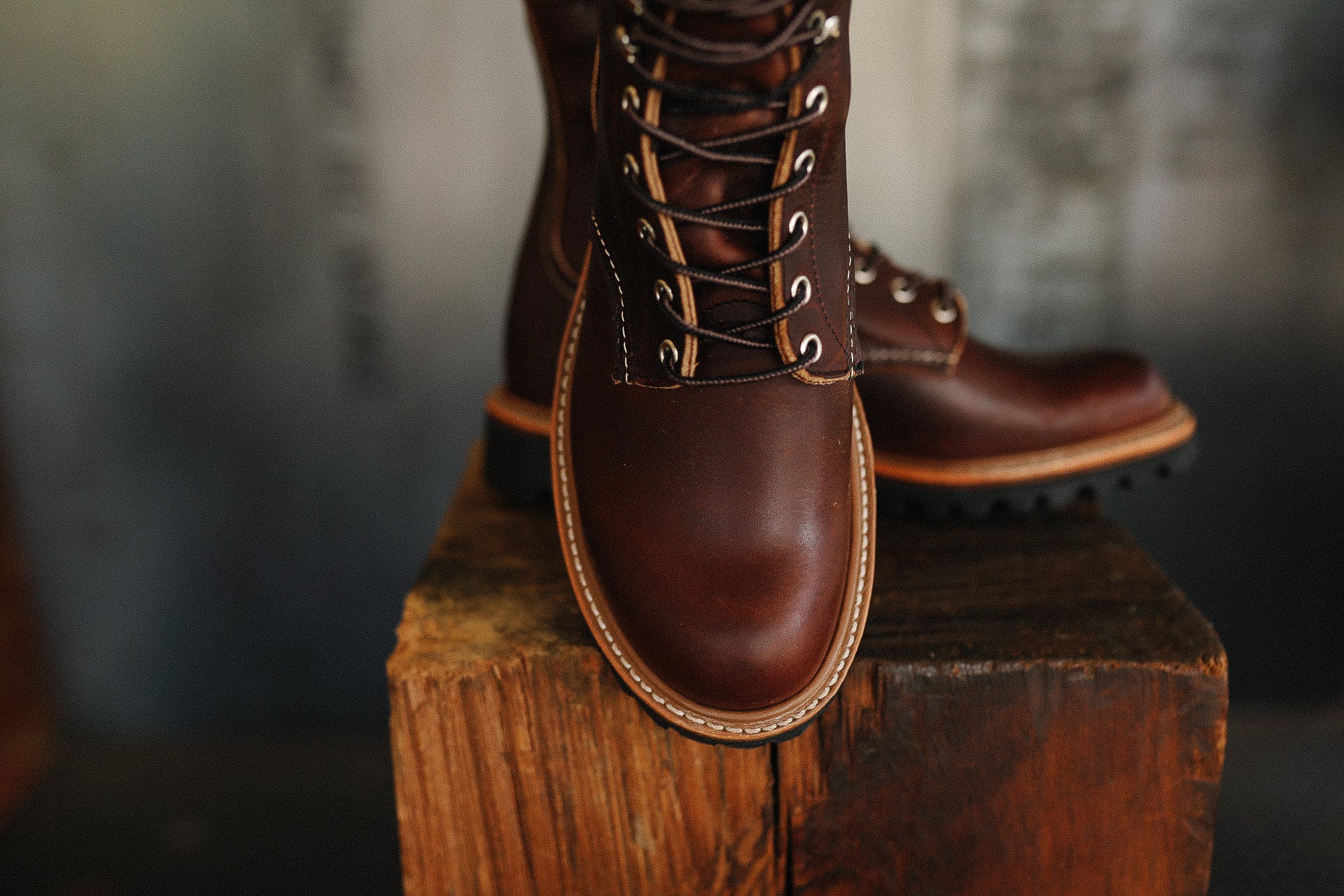 Close-up of handmade brown leather boots with black laces on rustic wooden block