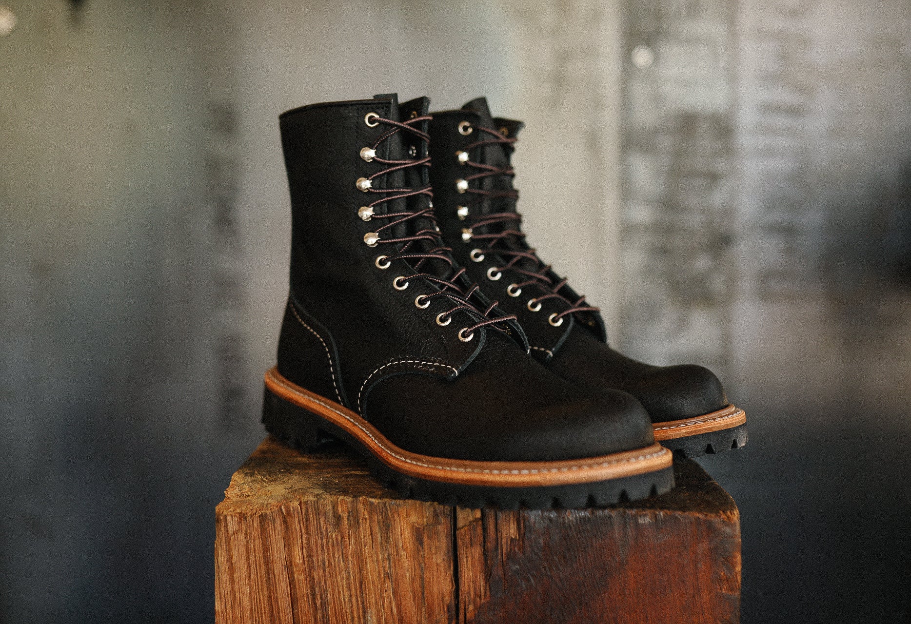 Pair of black leather lace-up boots with brown sole on rustic wooden block