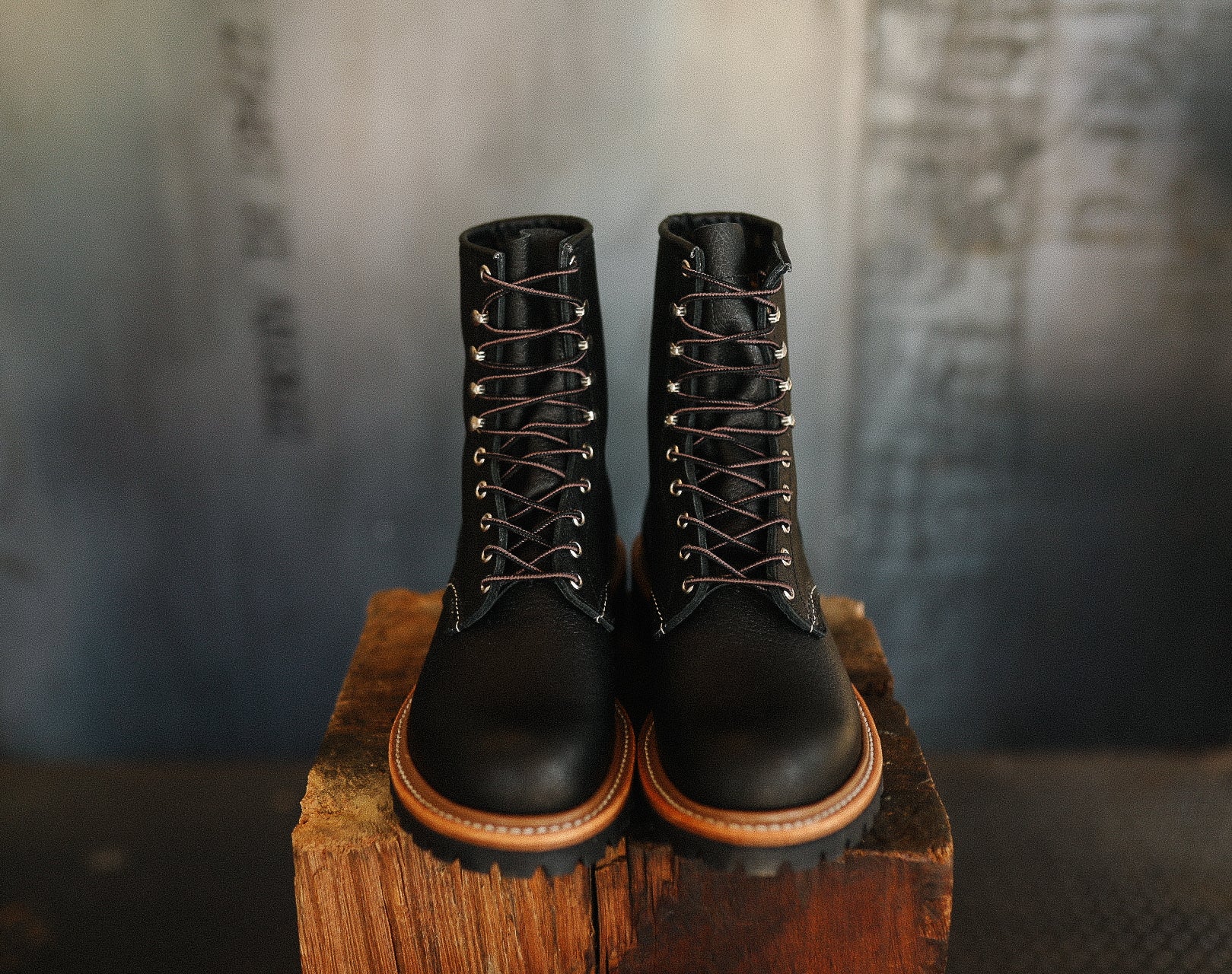 Black leather work boots with brown soles and laces on wooden block, industrial setting