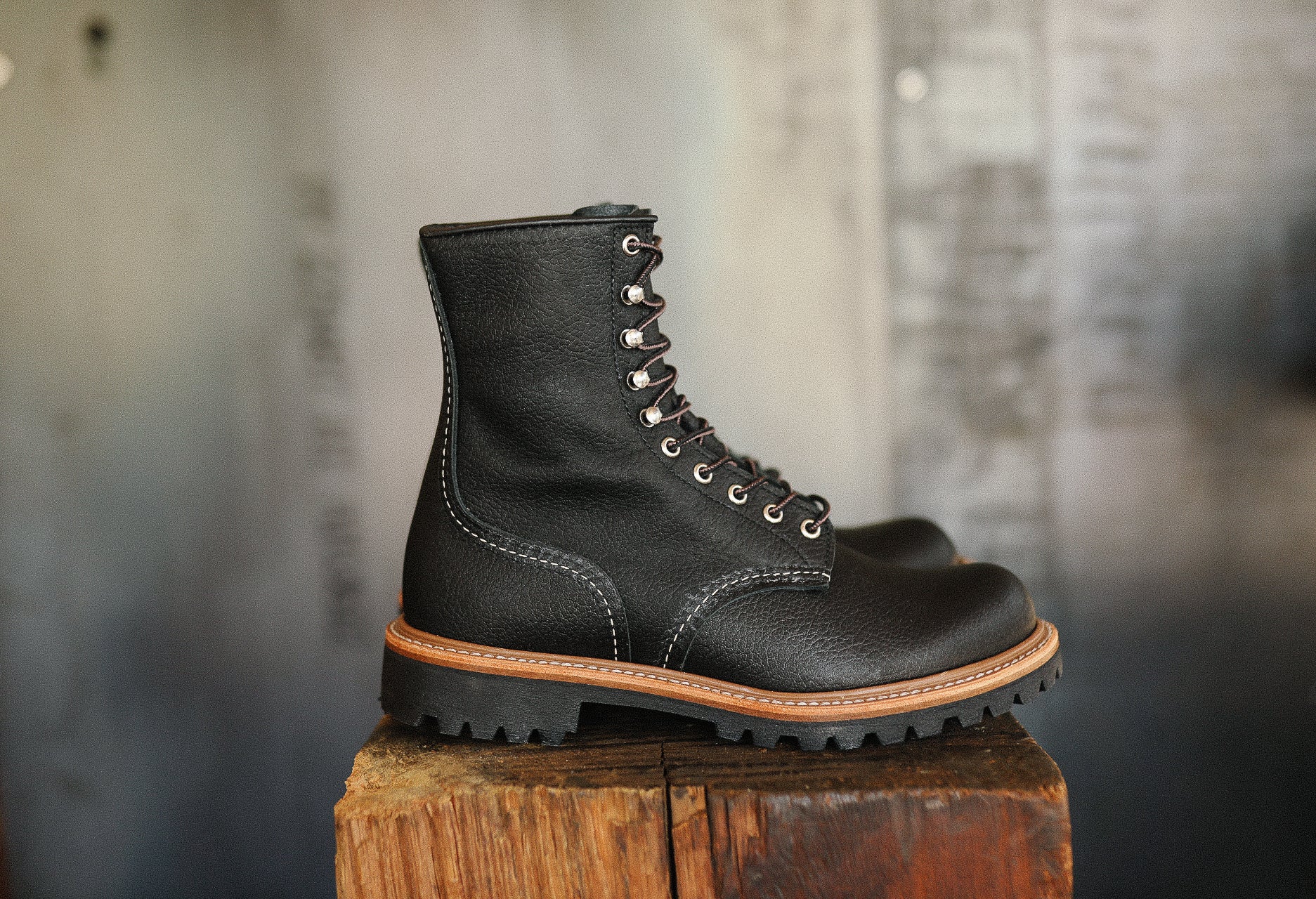 Black leather rugged work boot with thick sole and contrast stitching on wooden block