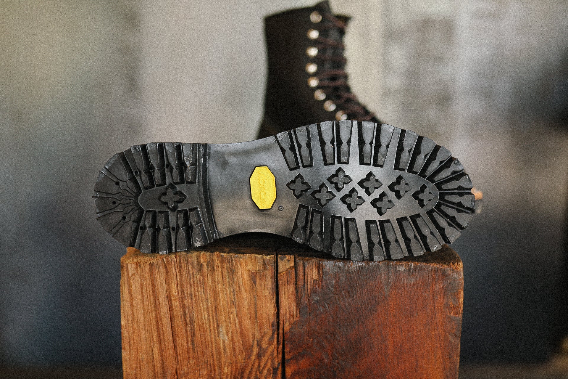 Black leather work boot with Vibram sole placed on rustic wooden block indoors
