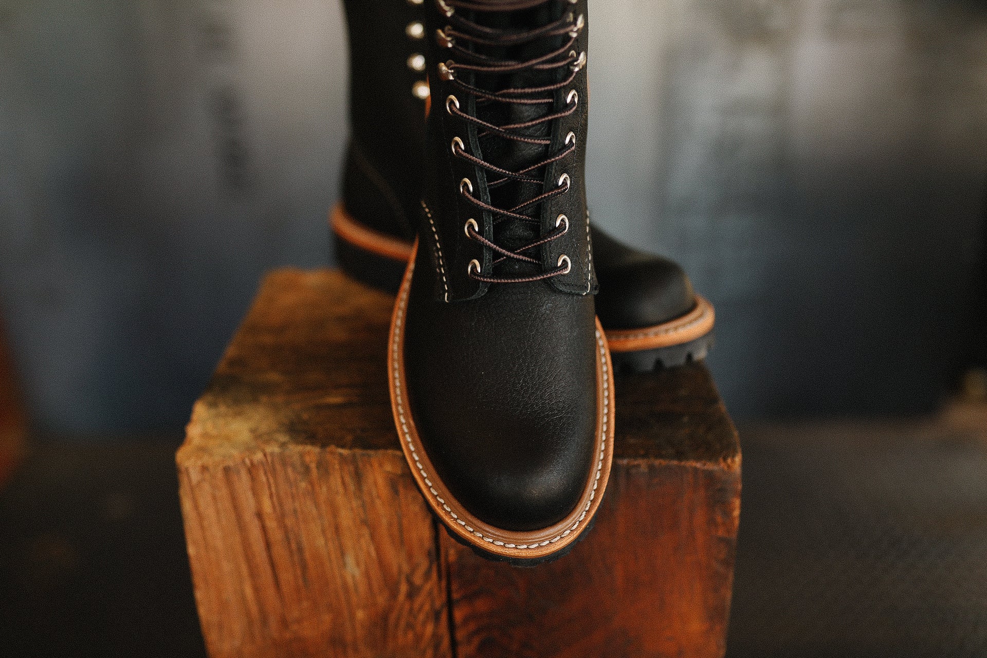 Close-up of black leather work boots with brown stitching on wooden block at Iron Shop Provisions