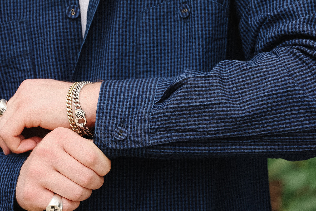 Close-up of a person's hands and arms wearing a dark blue and black checkered shirt, a silver chain bracelet, and rings.