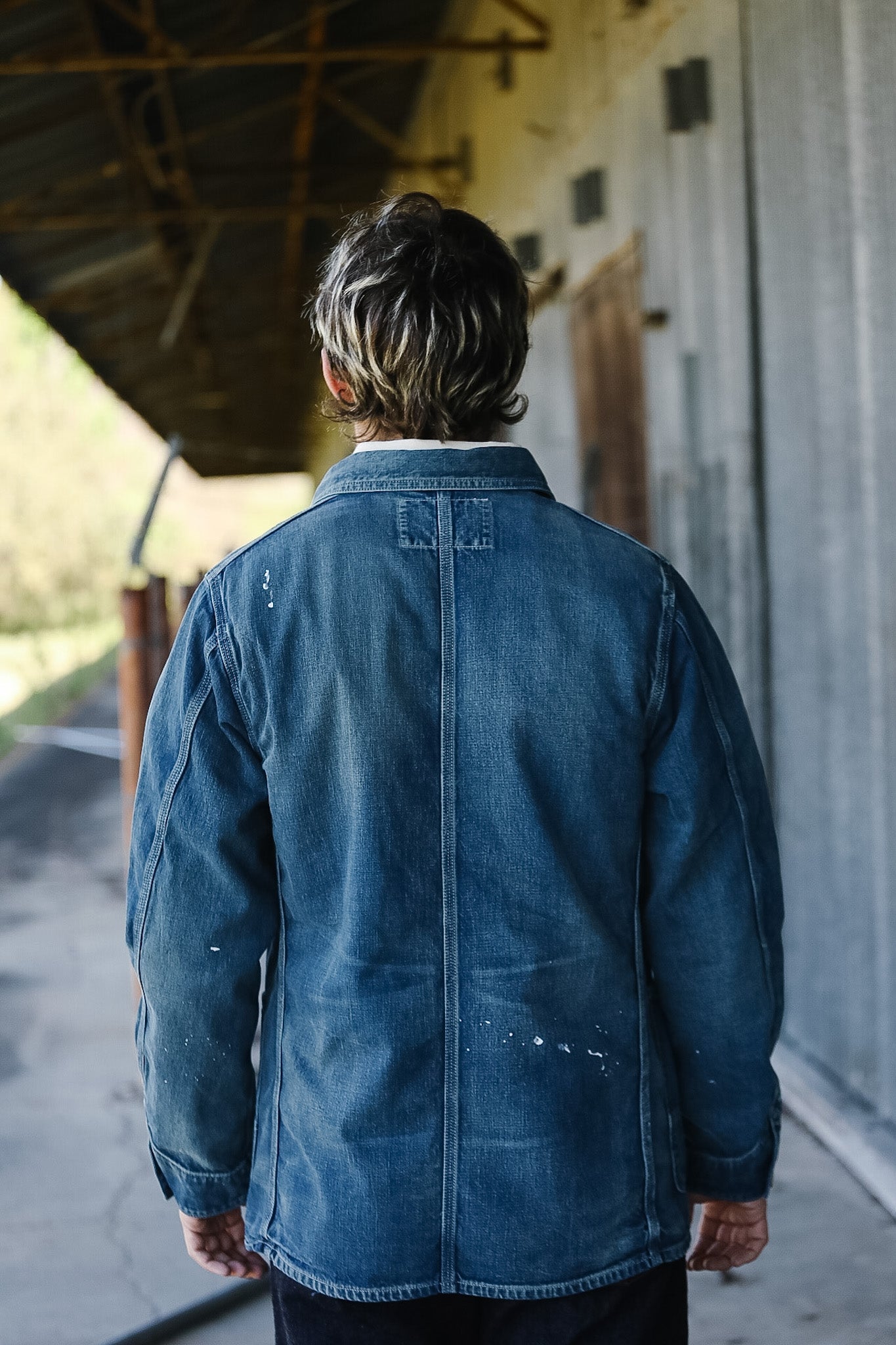 Person wearing a blue denim jacket standing in an outdoor setting.