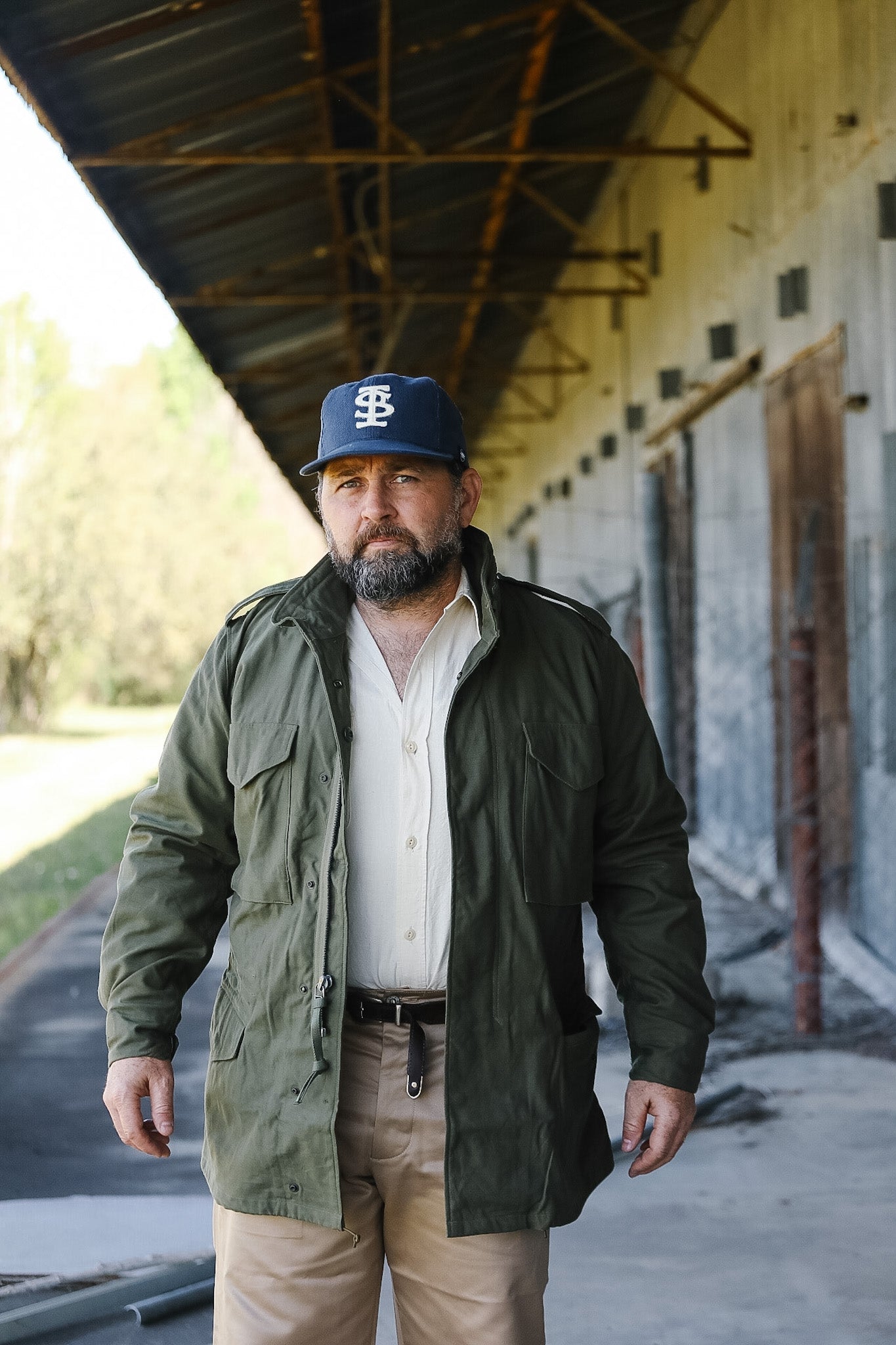 Man wearing a green jacket and cap standing in an industrial setting