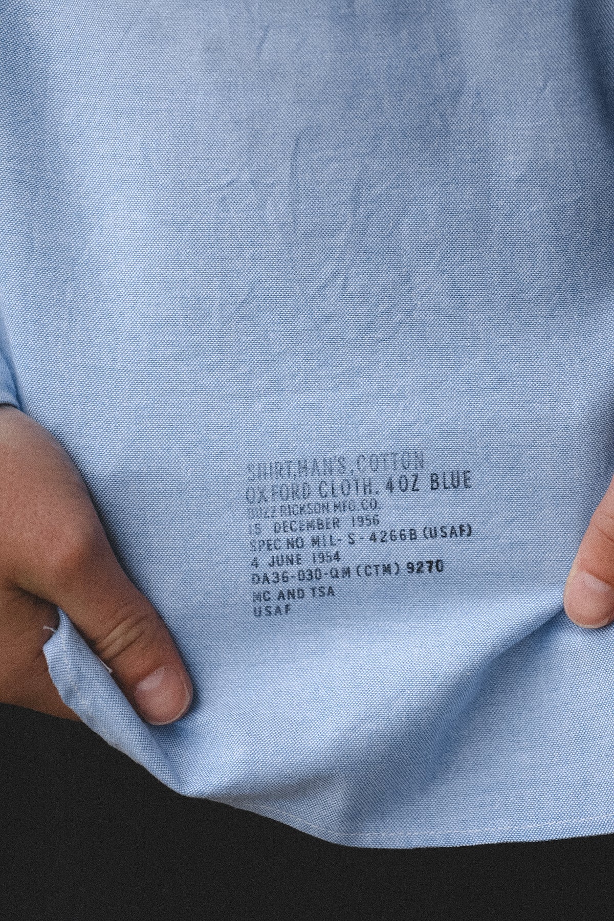 Close-up of a light blue shirt with text on the fabric, held by a person.