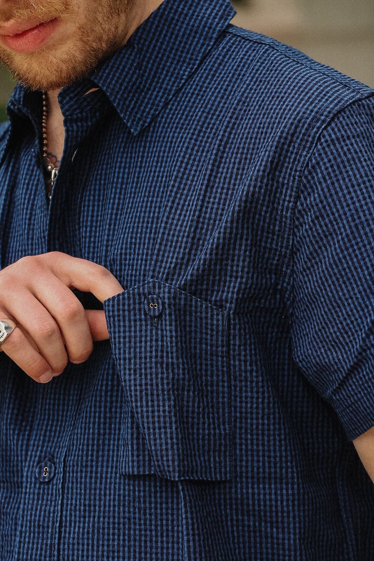 Close-up of a man wearing a short-sleeve button-up shirt with a small blue and white gingham pattern, adjusting the pocket flap.