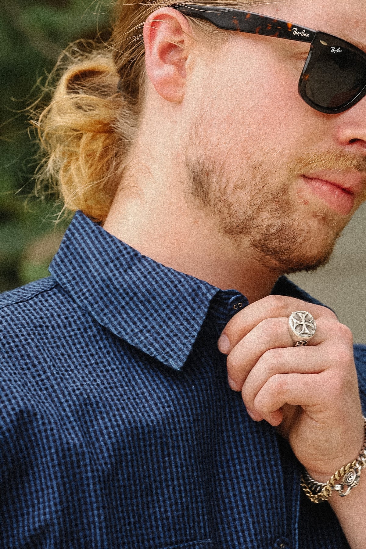 Close-up of a man wearing a dark blue and white checkered button-down shirt, black sunglasses, and a silver  ring.